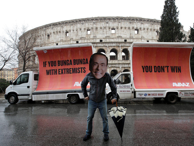 إيطالي يرتدي قناعاً لبرلوسكوني أمام الكوليزيون بروما أمس وخلفه لافتة كتب عليها «إذا كنت ستلعب مع المتطرفين فلن تفوز (رويترز)