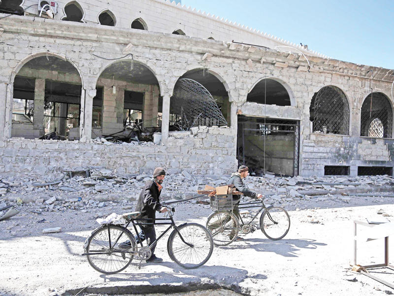 سوريان يسيران وسط الدمار في حمورية بالغوطة أمس (أ ف ب)