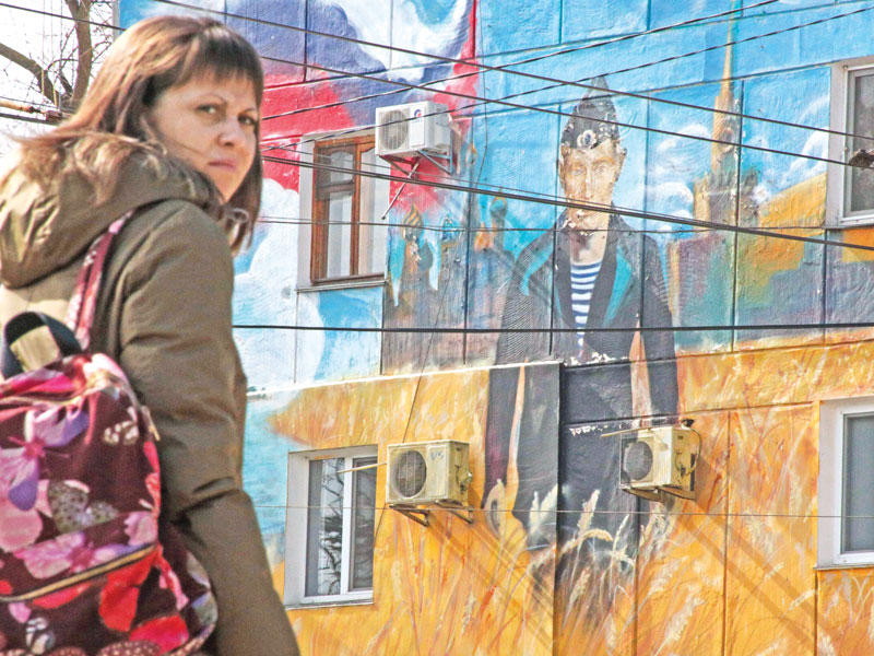 روسية تمر أمس في مدينة سيفاستوبول في القرم أمام جدارية لبوتين بزي البحرية الروسية (أ ف ب)