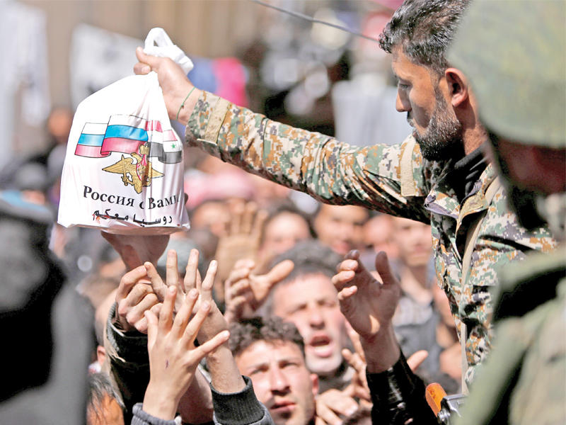 في مفارقة، جندي موالٍ للنظام يوزع مواد تموينية روسية على السكان الخارجين من الحصار السوري الروسي على الغوطة          (رويترز)