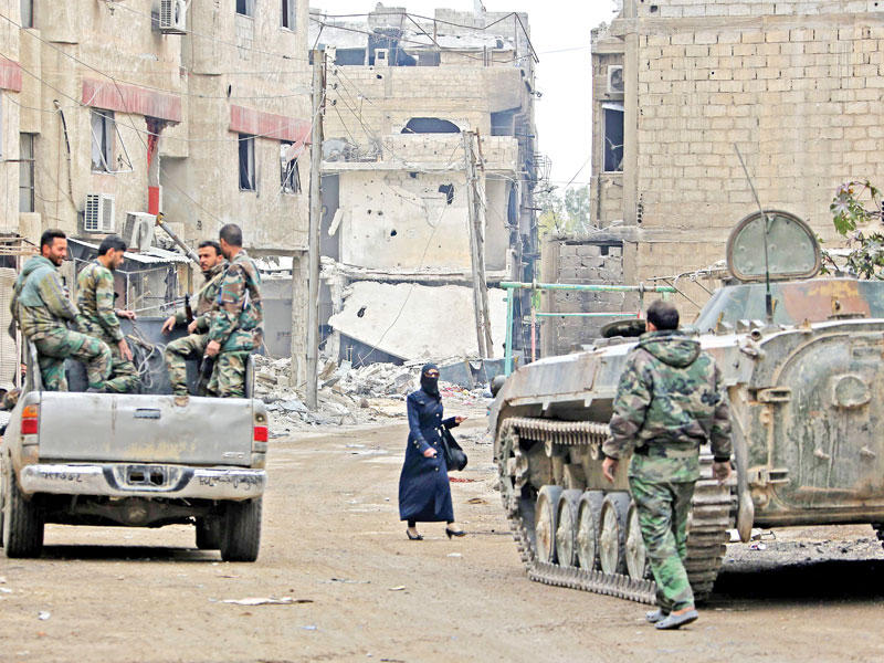 امرأة سورية تمر وسط جنود النظام في بلدة الهزاع قرب دوما أمس    (أ ف ب)