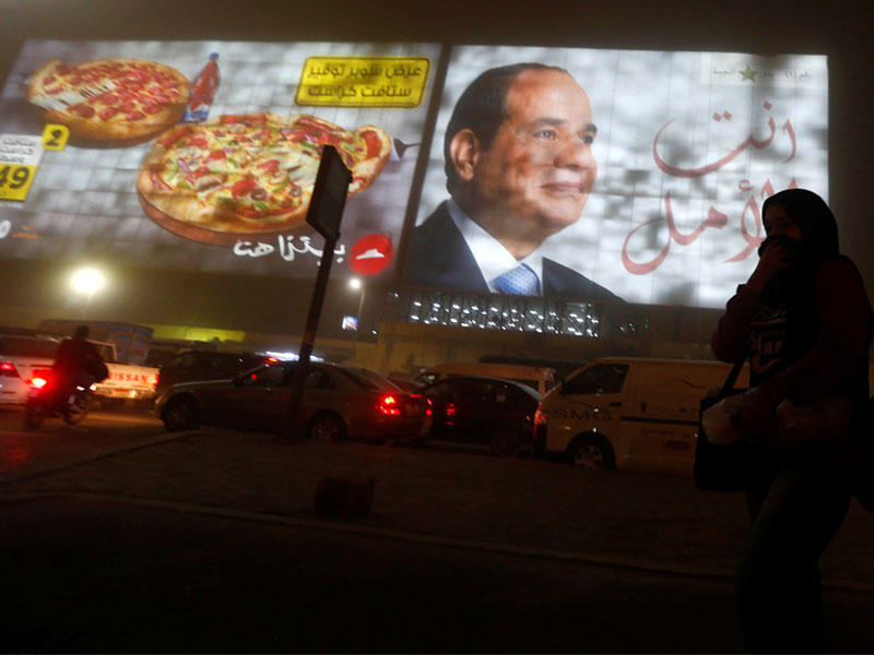 مصرية تمر أمام لافتة مؤيدة للسيسي وسط العاصفة الرملية التي ضربت القاهرة مساء أمس الأول (رويترز)