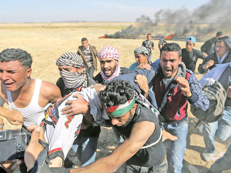 فلسطينيون يسعفون الشاب تحرير أبو سبلة (17 عاما) وهو أصم بعد إصابته خلال مواجهات مع الإسرائيليين على الحدود مع غزة أمس (رويترز)