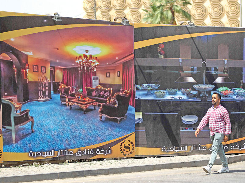 عراقي يمر قرب إعلان كبير لفندق جديد قيد الإنشاء في بغداد   (أ ف ب)