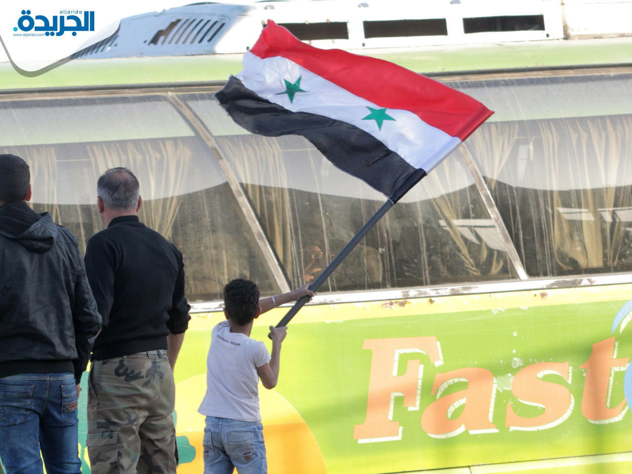 طفل يلوح بالعلم السوري أمام حافلات تجلي مقاتلي جيش الإسلام في دوما