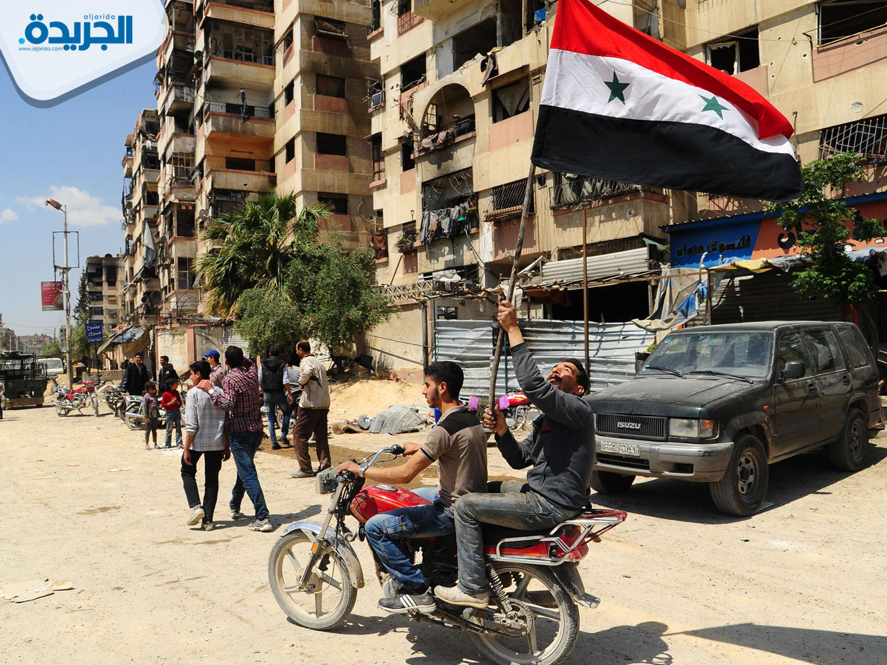 رجل يلوّح بالعلم السوري على ظهر دراجة نارية في أحد شوارع بلدة دوما