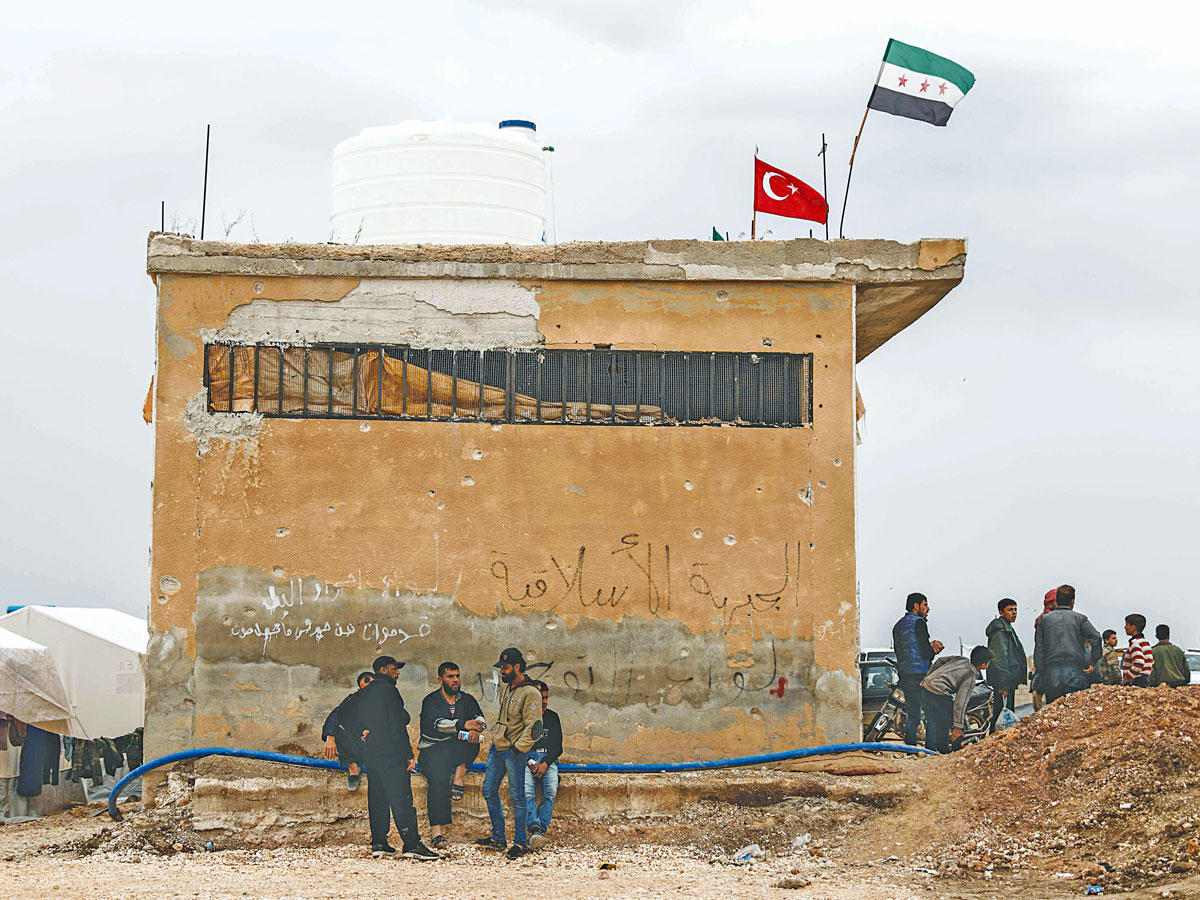 سوريون قرب مخيم للاجئين في اعزاز بإدلب التي تسيطر عليها فصائل تابعة لتركيا  (أ ف ب)