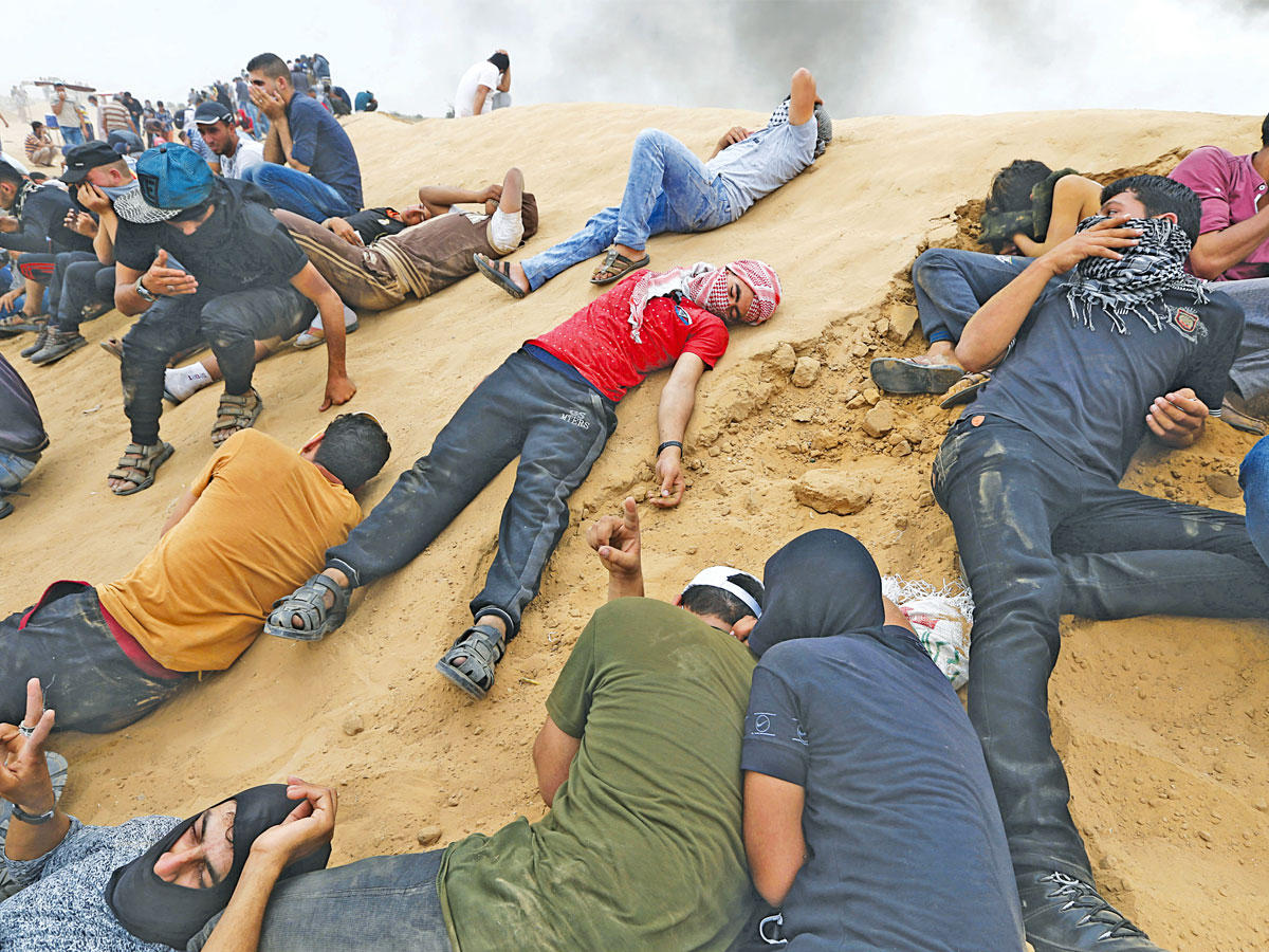 فلسطينيون يحاولون الاحتماء من قنابل الغاز المسيل للدموع خلال مواجهات على شريط غزة (رويترز)  