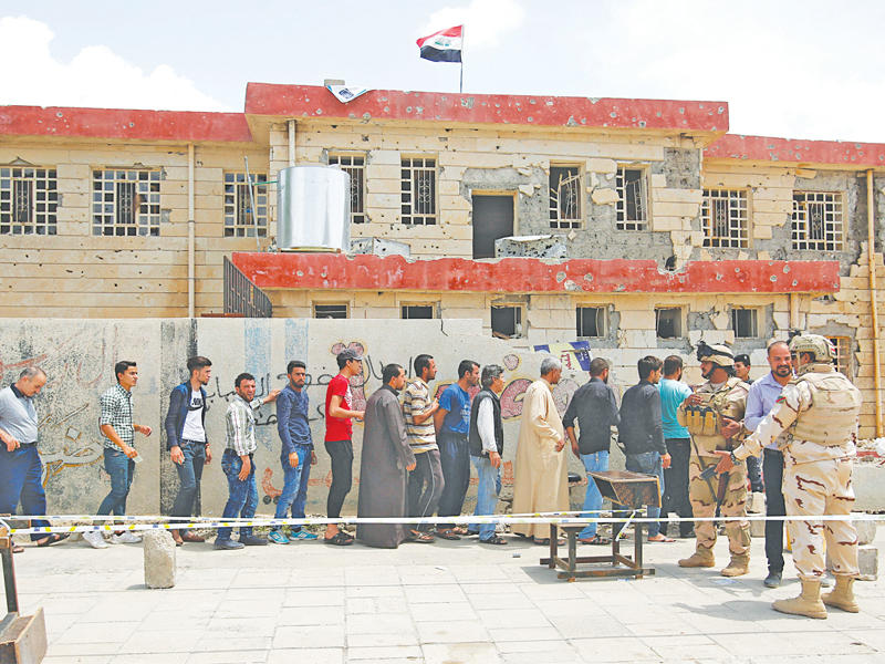مواطنون موصليون يقفون عند مركز انتخابي في إحدى المدارس ويبدو عليها آثار الدمار في الموصل أمس (رويترز)
