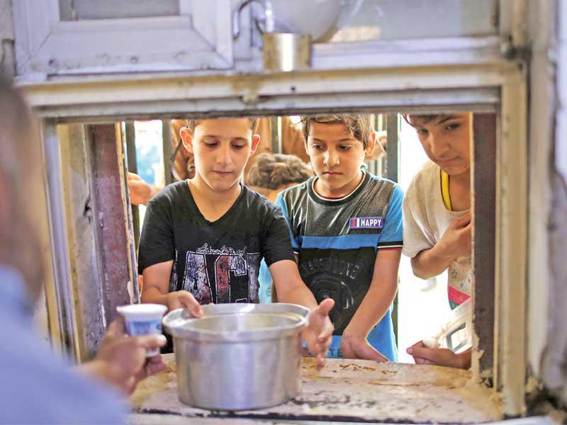 أطفال يأخذون حصتهم من الطعام في مقام عبدالقادر الكيلاني في بغداد قبل يومين (رويترز)