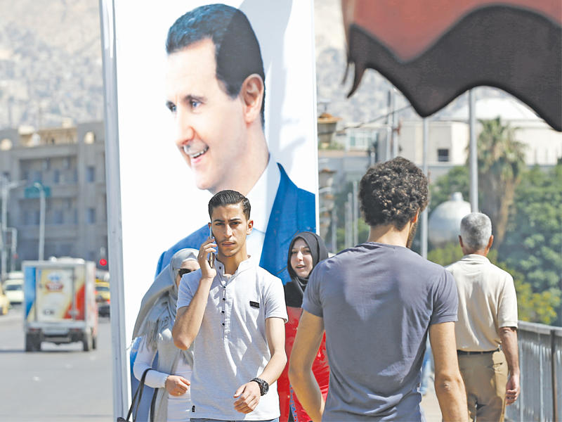 سوريون يمرون امام صورة للأسد في دمشق (أ ف ب)