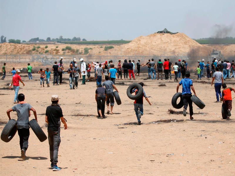 شبان فلسطينيون ينقلون إطارات السيارات لإشعالها قرب السياج الحدودي مع إسرائيل أمس (أ ف ب)