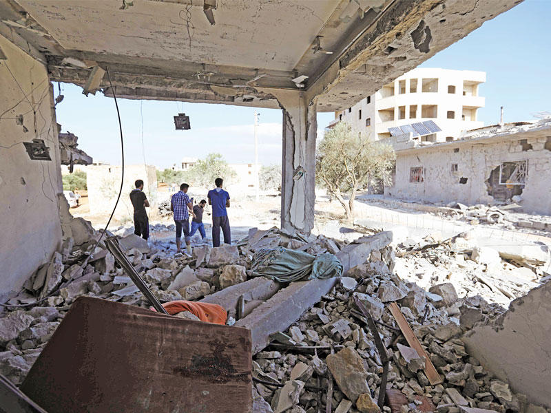 سوريون يتفقدون مبنى دمرته غارات النظام في بلدة بنش بإدلب أمس الأول (أ ف ب)