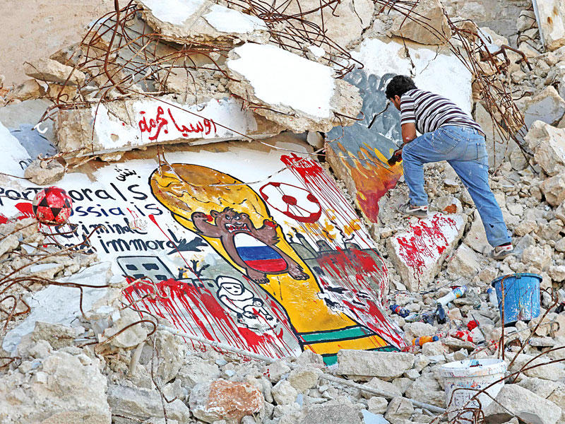 الرسام السوري عزيز الأسمر يضع اللمسات الأخيرة على جدارية معادية لروسيا واستضافتها كأس العالم على أنقاض مبنى مدمر في بلدة بنش بمحافظة إدلب يوم السبت (أ ف ب)