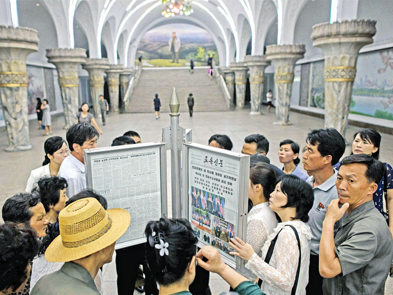 كوريون شماليون يتصفحون أمس بيونغ يانغ بطريقة مشتركة عبر نسخة من صحيفة «رودونغ سينمون» لمتابعة أخبار قمة سنغافورة  (أ ف ب)