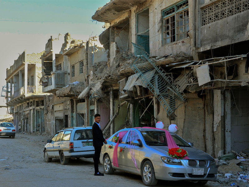 شاب عراقي يقف بجوار سيارة مزينة لأول حفل زفاف في مدينة الموصل القديمة بعد عام من استعادتها من قبل قوات الحكومة العراقية