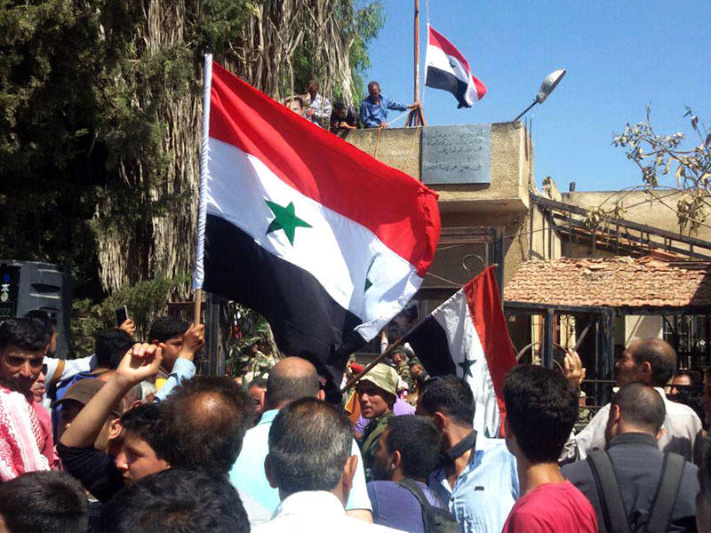 رجال سوريين يلوحون بعلمهم الوطني بالقرب من مجلس المدينة بعد أن استعادت قوات النظام السوري مدينة طفس