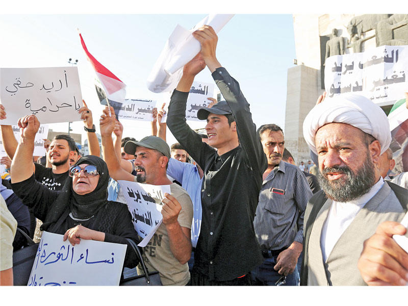 عراقيون بينهم رجل دين خلال تظاهرة في ساحة التحرير ببغداد أمس الأول (إي بي أيه)