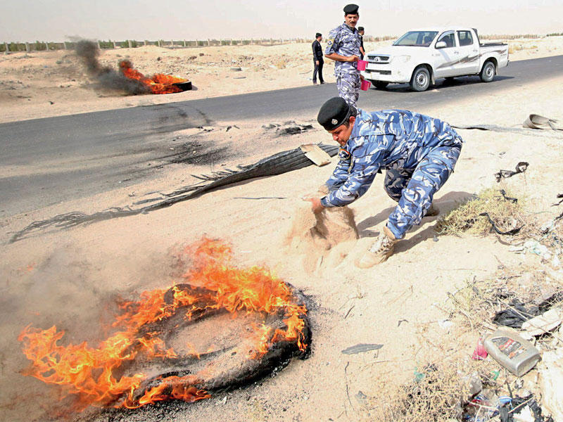 شرطي عراقي يحاول إطفاء إطار سيارة مشتعل في الزبير أمس (رويترز)