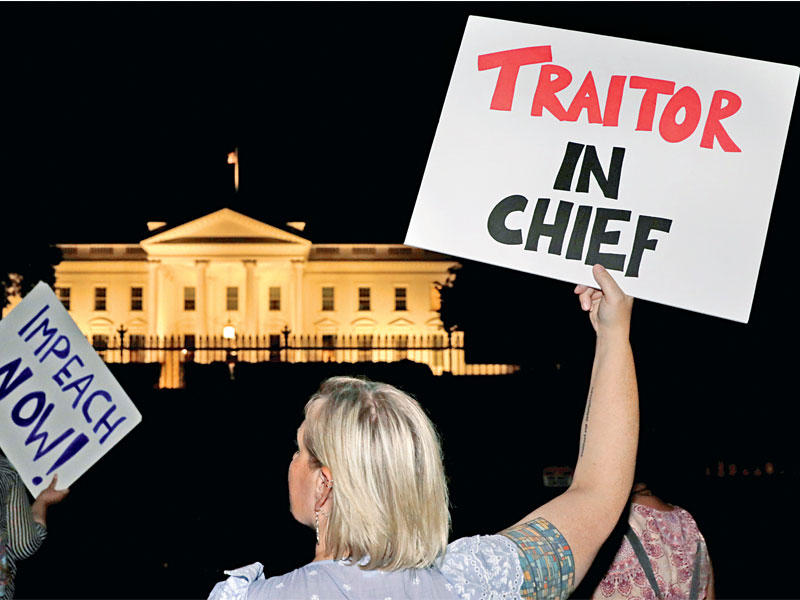 متظاهرة خارج البيت الأبيض ترفع لافتة تتهم ترامب بالخيانة مساء أمس الأول (رويترز)