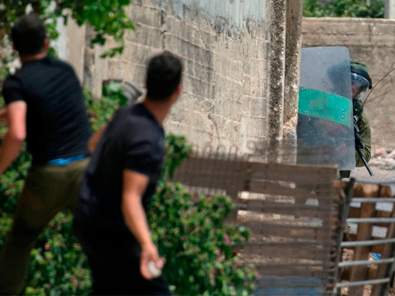 جندي إسرائيلي يحتمي خوفاً من حجارة شبان فلسطينيين خلال مواجهات في الضفة الغربية أمس (ا ف ب)