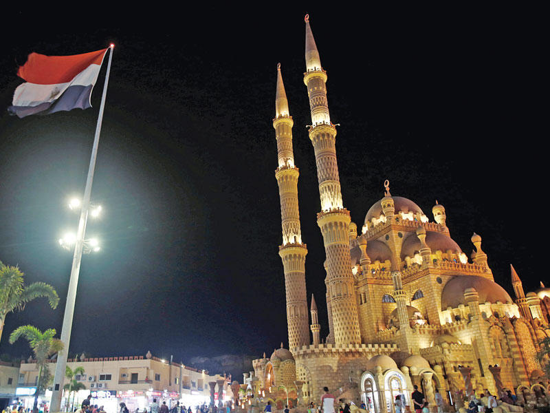 مصريون وسياح يمرون أمام مسجد الصحابة في منطقة السوق القديم في شرم الشيخ (رويترز)