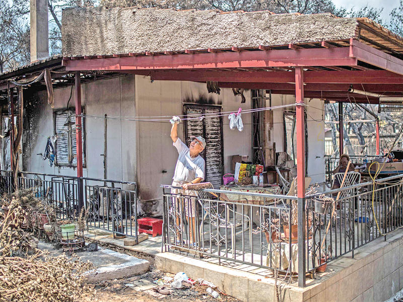 يوناني ينظف منزله الذي تضرر بفعل الحرائق في قرية نيوس فوتزاس أمس (ا ف ب)