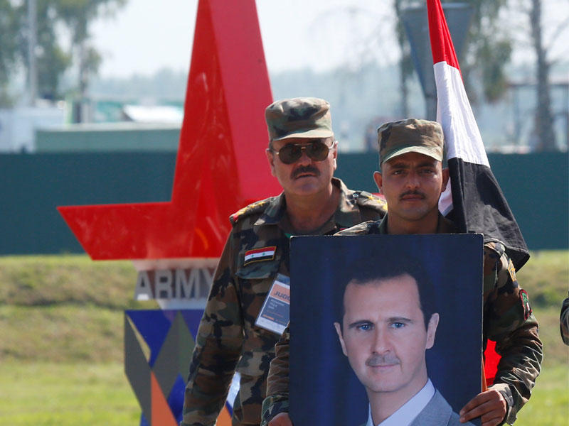 جندي سوري يحمل صورة الأسد خلال افتتاح الألعاب العسكرية لعام 2018 في الابينو خارج موسكو أمس الأول (رويترز)