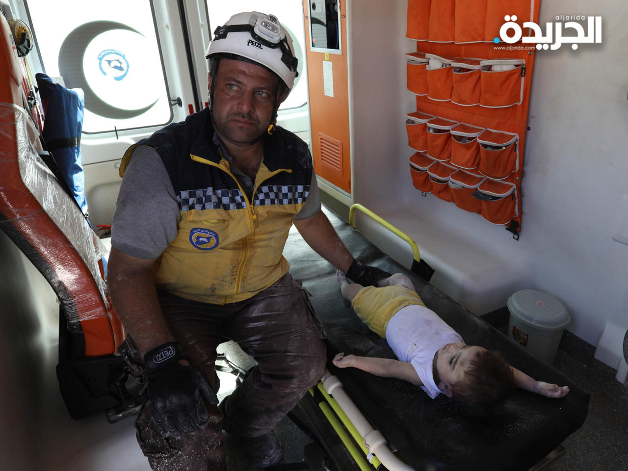 عامل من فريق ذوي الخوذات البيضاء بجانب جثمان طفل عقب انفجار في مستودع للأسلحة في منطقة سكنية بإدلب