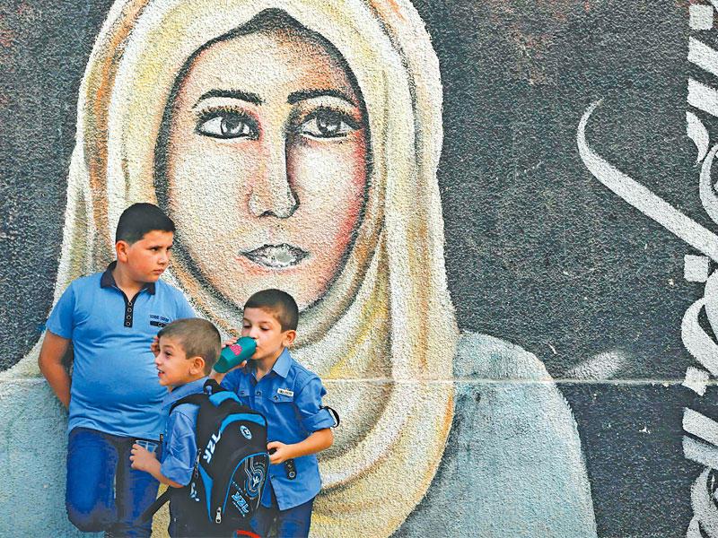 أطفال فلسطينيون أمام رسمة على جدار مدرسة تابعة لـ«أونروا» في غزة أمس                        (أ ف ب)