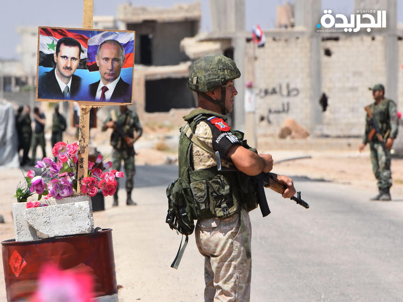 جندي روسي وآخر روسي يقفان بالقرب من ملصق الرئيس السوري ونظيره الروسي عند معبر أبو ضهور على الطرف الشرقي من محافظة إدلب