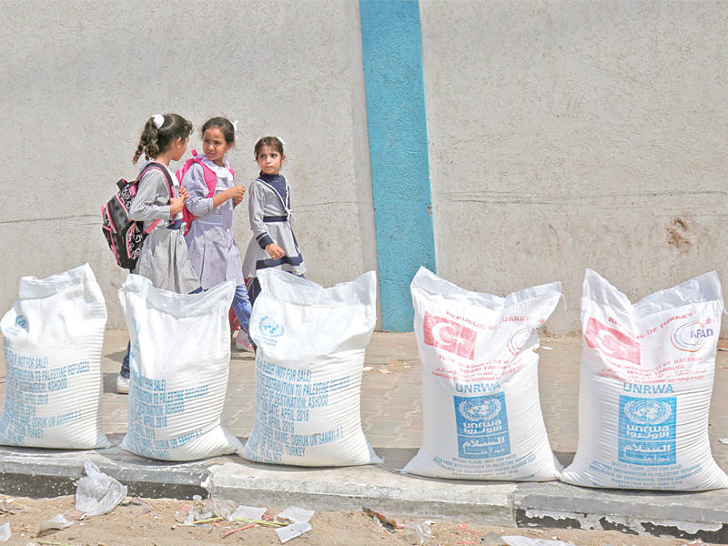 تلميذات في مخيم رفح بغزة خلال مرورهن بالقرب من أكياس طحين مقدّمة من الأمم المتحدة أمس (أ ف ب)