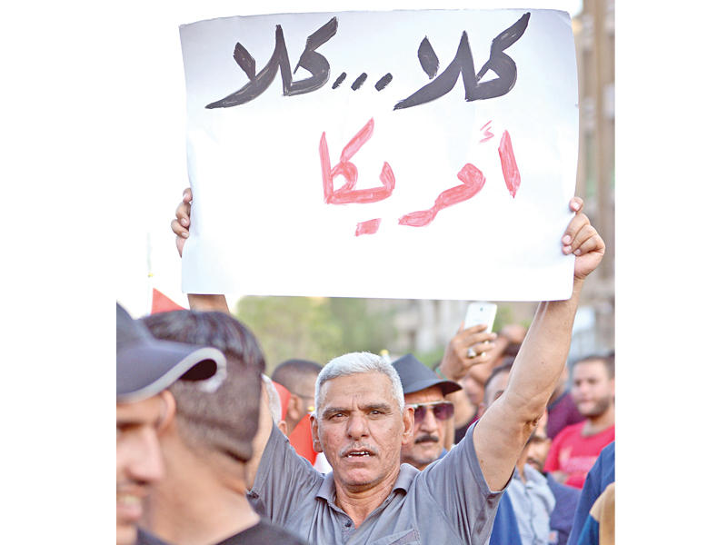عراقي يرفع لافتة مناهضة للولايات المتحدة خلال تظاهرة وسط بغداد أمس الأول (إي بي أيه)