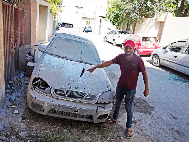 ليبي قرب سيارة متضررة بفعل الاشتباكات في مدينة بن عاشور في طرابلس أمس الأول	 (اي بي آي)