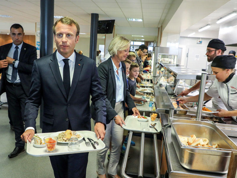 ماكرون يحمل الطعام بمقصف مدرسة في لافال أمس الأول (رويترز)