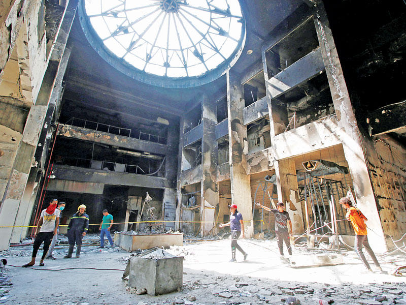 عمال ينظفون أمس مقر محافظة البصرة الذي أحرقه متظاهرون قبل أيامt (رويترز) 