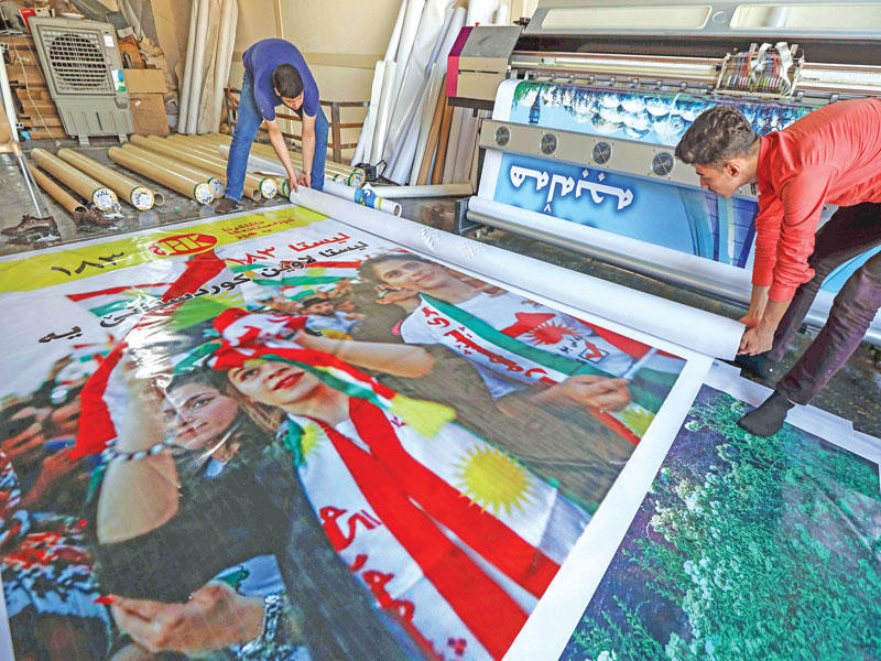 عاملان يعدان ملصقات دعائية للمرشحين بانتخابات كردستان في أربيل أمس (أ ف ب)