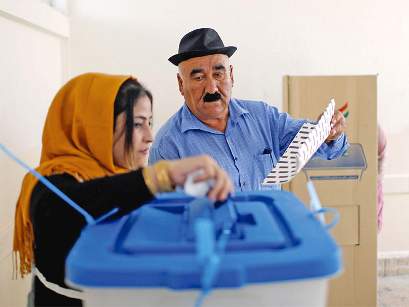 موظفة تساعد رجلاً كردياً على الإدلاء بصوته في أربيل أمس  (رويترز)