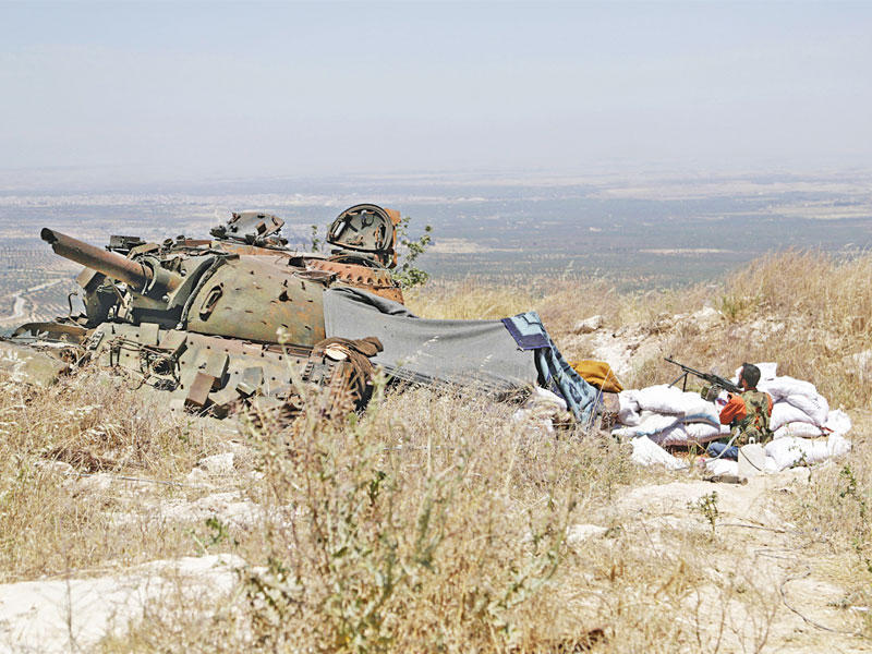 مقاتل معارض إلى جانب دبابة معطوبة في إدلب (رويترز)
