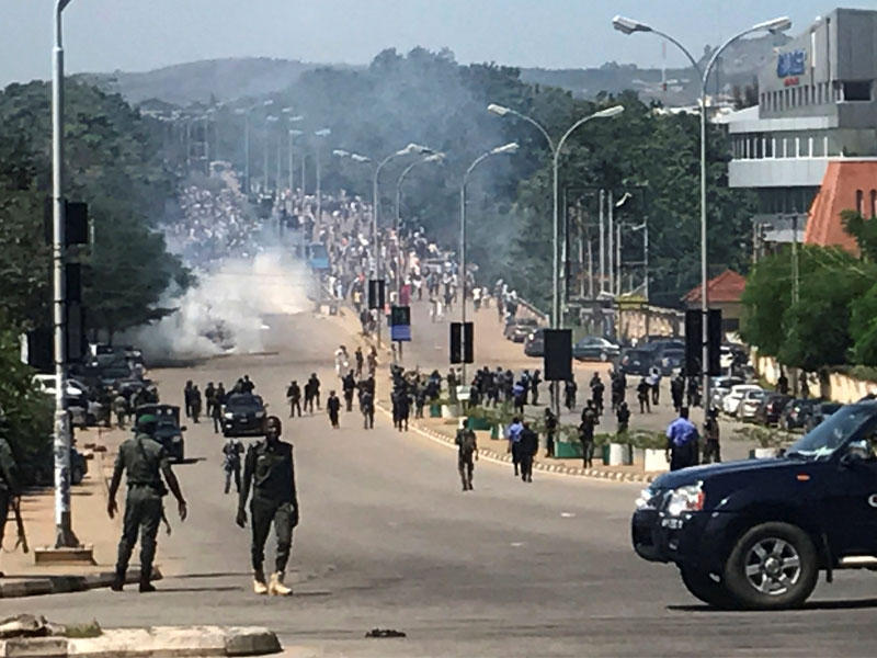 يتم نشر أفراد من قوات الأمن كما شوهد الدخان في الخلفية خلال مسيرة من قبل المتظاهرين الحركة الإسلامية في نيجيريا