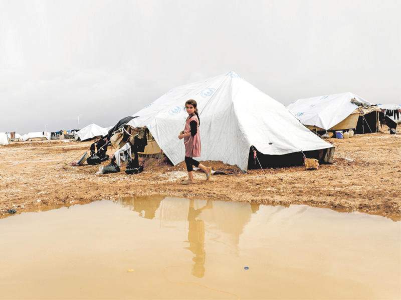 فتاة سورية تمر أمام تجمع للأمطار في مخيم بالحسكة للمهجرين من دير الزور (أ ف ب)