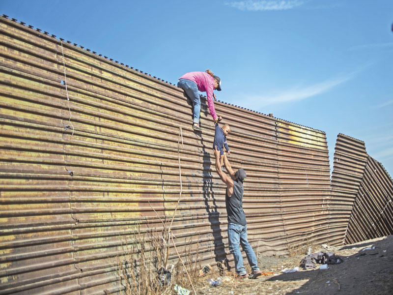 لاجئان يحاولان مع طفلهما عبور جدار مرتفع على الحدود المكسيكية إلى أميركا   (أ ف ب)