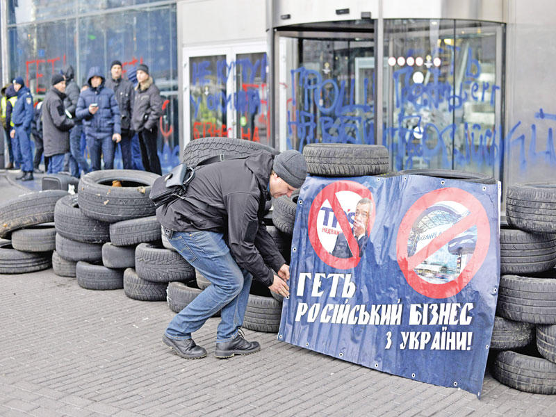 أوكراني أمام لافتة تدعو إلى وقف التعاملات التجارية مع روسيا بواجهة مركز التسوق «أوشين بلازا» في كييف أمس (أ ف ب)