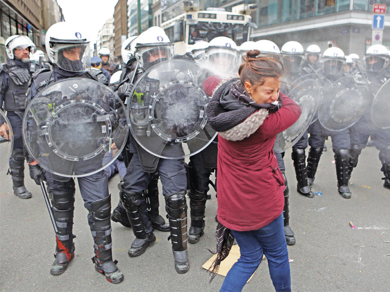 سيدة تحاول الاحتماء من الغاز المسيل للدموع خلال مواجهات مع الشرطة في بروكسل أمس (ا ف ب)