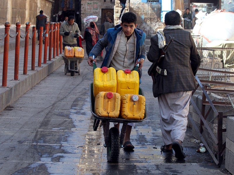يمني يدفع عربة يدوية بالعبوات المملوءة بالماء من مصدر تم التبرع به في الحي القديم من صنعاء