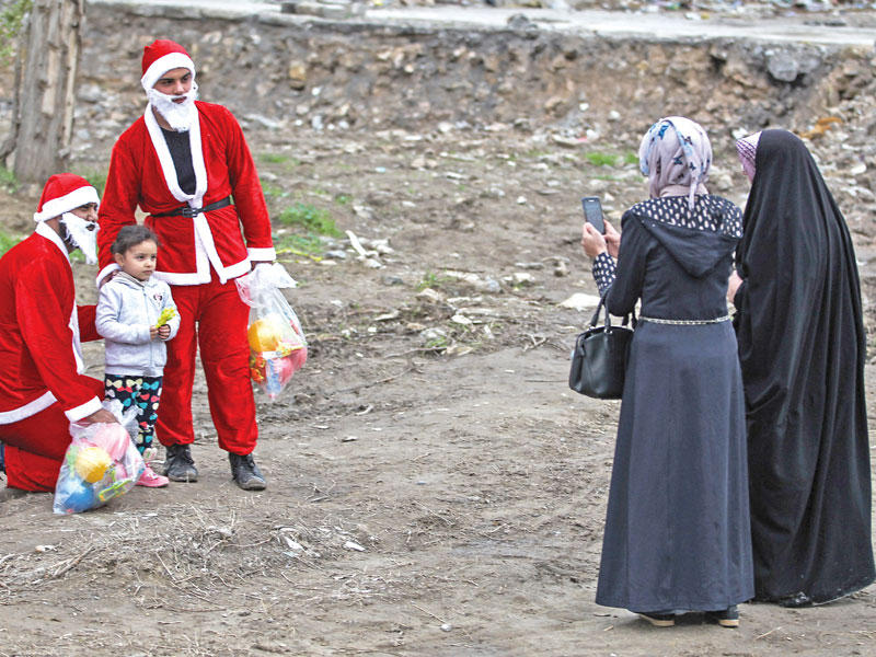 عراقيتان تأخذان صورة لطفل مع شخصين يرتديان زي سانتا في الموصل قبل أيام (أ ف ب)