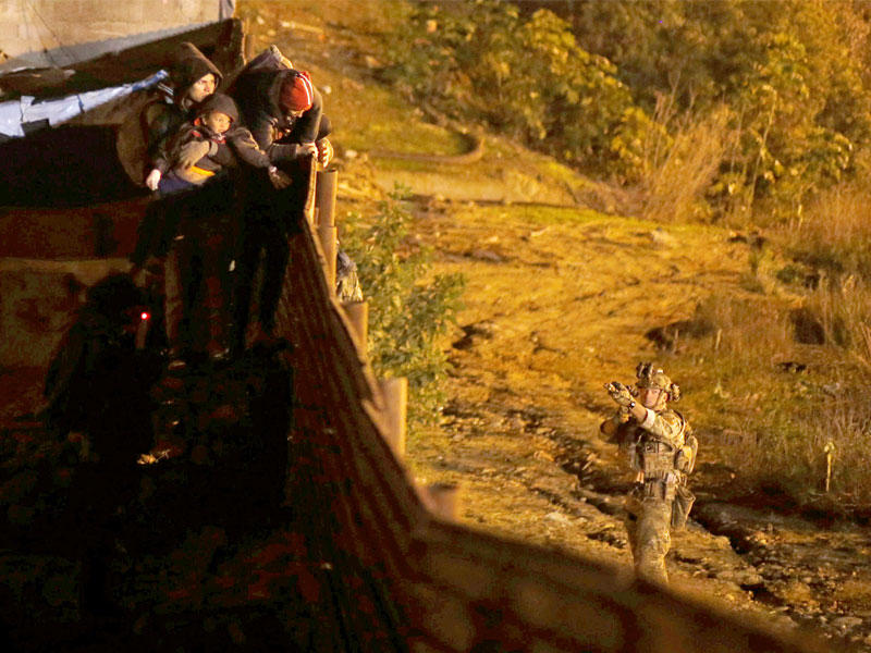 جندي أميركي يصوّب بندقيته تجاه مجموعة مهاجرين لمنعهم من عبور الحدود المكسيكية أمس الأول (رويترز)