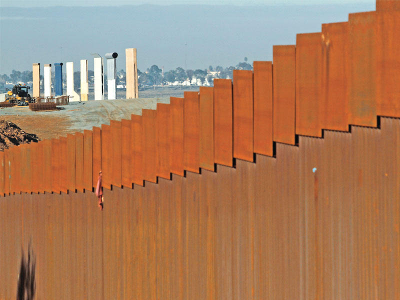 جزء من السياج الحدودي في تيخوانا بين أميركا والمكسيك وتبدو في الخلفية عينات جدران مصنوعة بمواد بناء مختلفة ستعرض على ترامب خلال زيارته للحدود (رويترز)