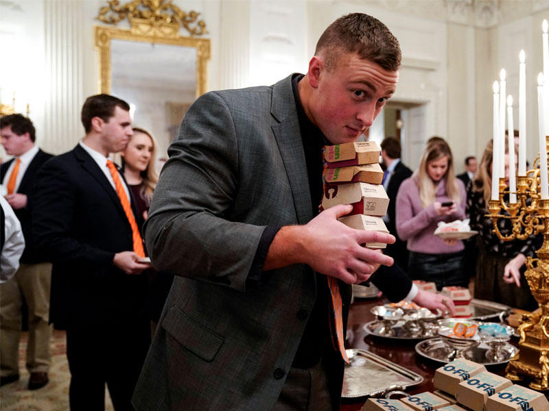 لاعب من «نمور كليمسون» يحمل ما أمكن من البرغر خلال العشاء في البيت الأبيض أمس الأولt (رويترز)