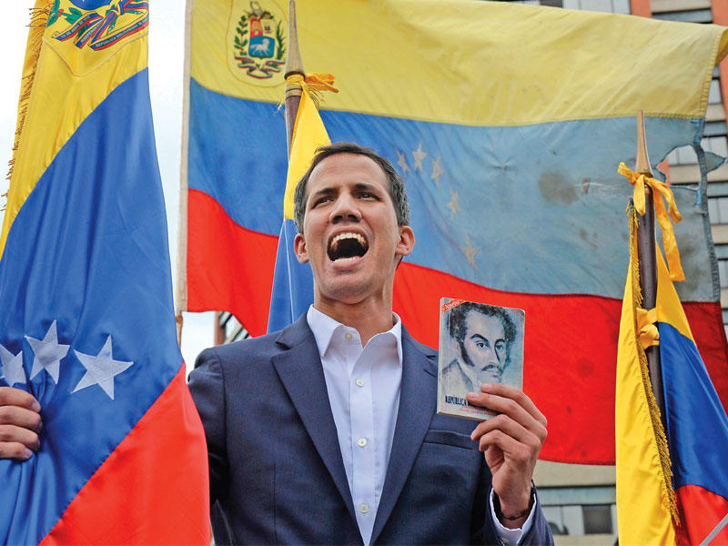 غوايدو رافعاً صورة مفجّر الثورة البوليفارية سيمون بوليفار وممسكاً بالعلم الفنزويلي (أ ف ب)n